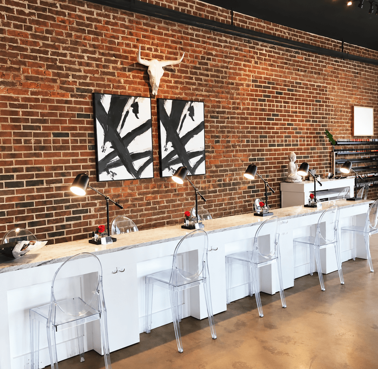 Manicure stations with clear chairs and an exposed brick wall at the Columbia studio