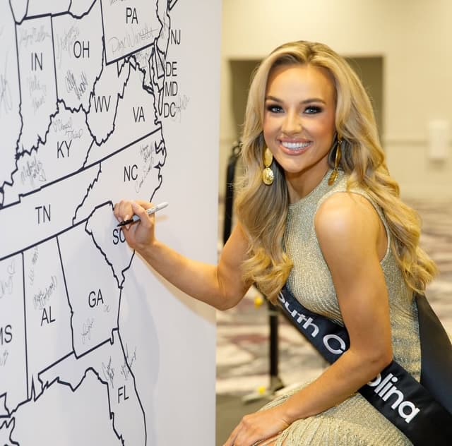 Woman wearing a South Carolina sash signing South Carolina on a state map