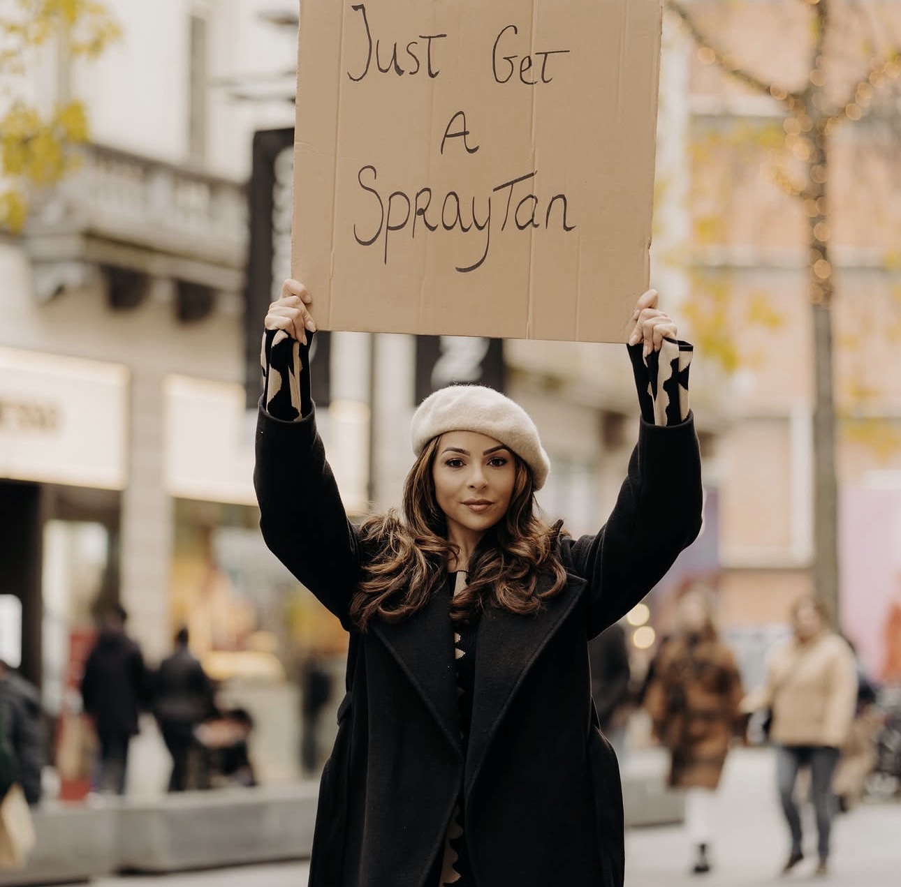 Gigi wearing a beret and holding a Just Get A SprayTan sign