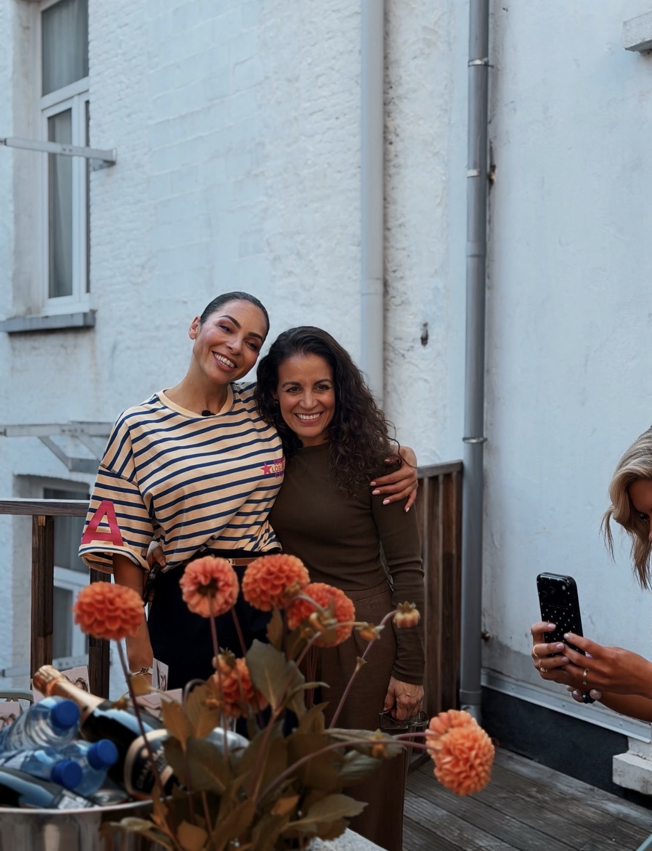 Two women smiling together on a flower-filled terrace