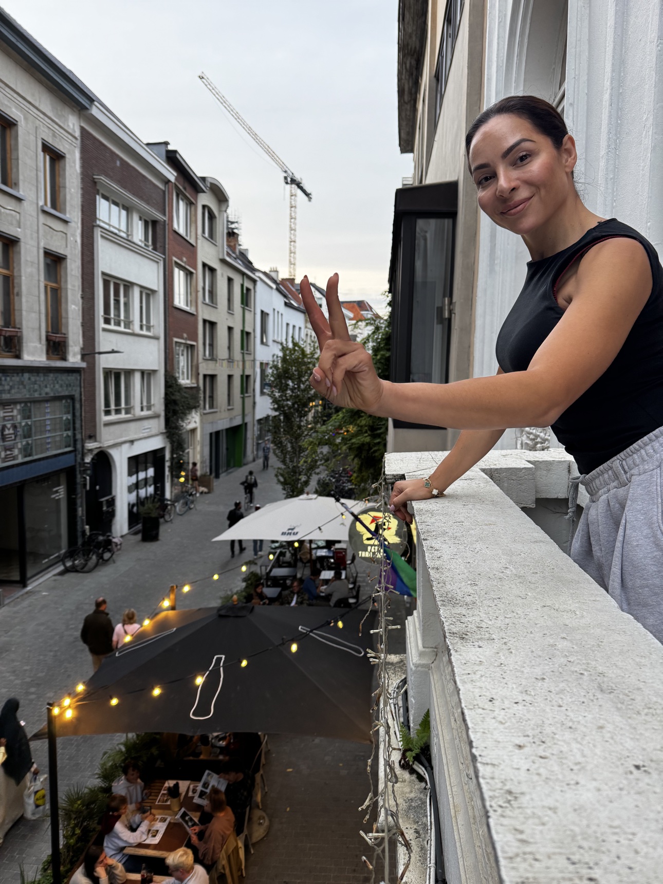 A woman smiling and giving a peace sign from an Antwerp balcony