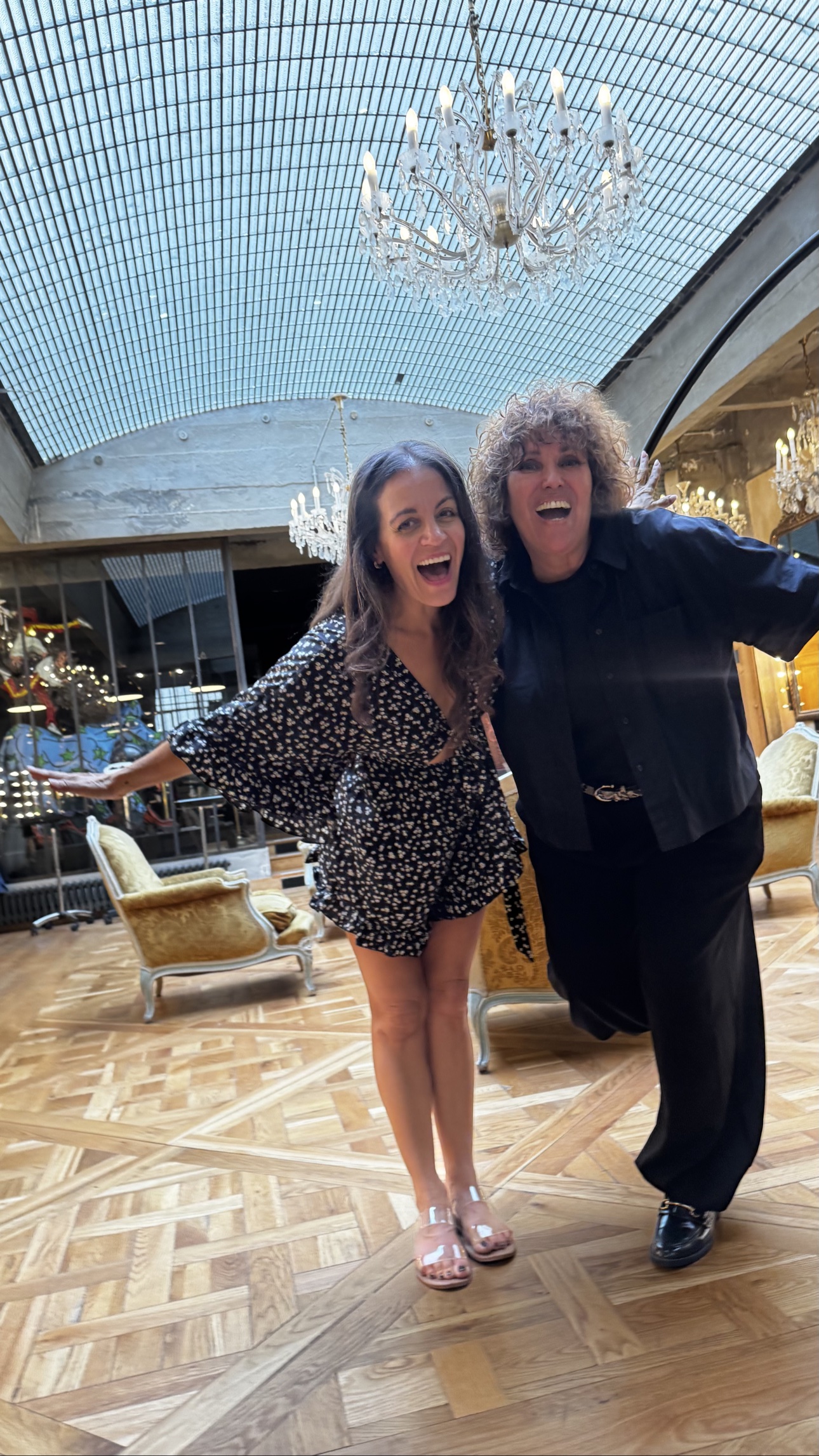 Two friends laughing together beneath a chandelier